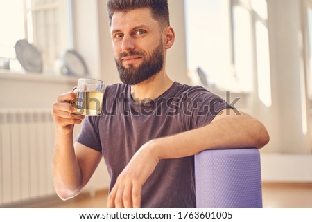 Handsome male looking at camera and smiling while holding glass cup of hot drink
