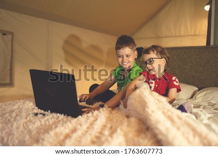 Two children watch cartoons on a laptop while sitting on a bed in a tent house