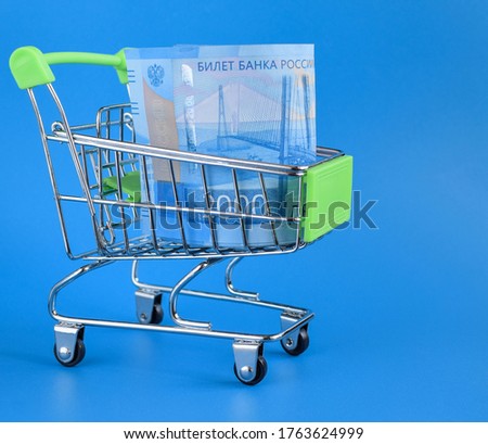 Russian rubles in a trolley on a blue background. Grocery basket and 2000 ruble bills. Russian currency. Side view. Selective focus. Copy space.