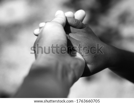 The hand of a child with dark skin rests on the hands of an adult with light skin.