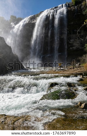 Tourist in a yellow jacket relaxing at the Tortum waterfall in Turkey. A young man traveler standing on a rock with his hands wide open at Tortum Waterfall in Erzurum, Turkey Royalty-Free Stock Photo #1763697890