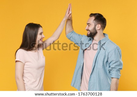 Smiling young couple two friends guy girl in pastel blue casual clothes posing isolated on yellow background. People lifestyle concept. Mock up copy space. Giving high five, looking at each other