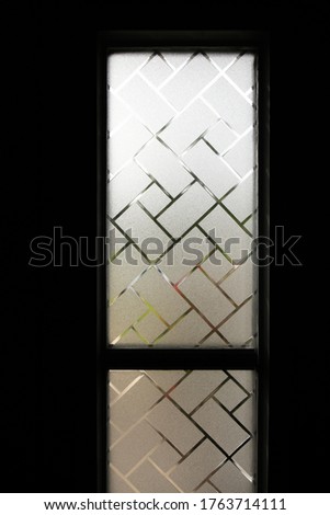 Two window panes coated with privacy screens in a dark room with light streaming in