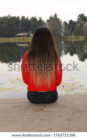 woman with long blond hair, girl wearing red sweater, sitting by the lake.