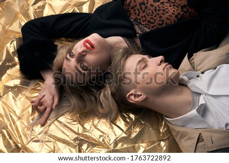 Stylish couple posing on a golden background from a foil lying.