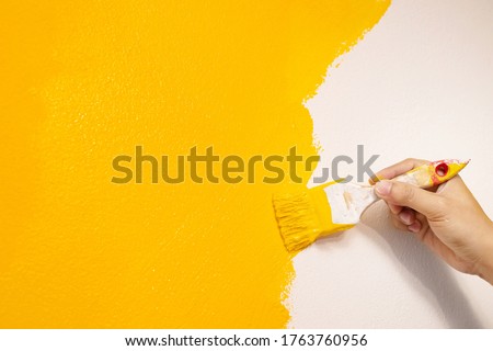 Paint brush, close up hand painter worker painting on surface wall Painting apartment, renovating with yellow color paint. Leave empty copy space to write descriptive text beside.