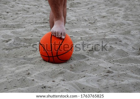 The young man put his foot on the basketball. The man holds the ball with his foot. Bottom view. Vacation, beach, summer.