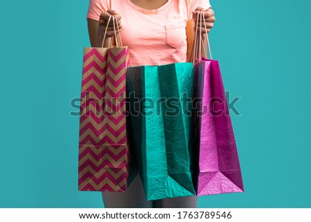 Cropped shot of female hands holding a bunch of paper shopping bags. Isolated over blue background.
