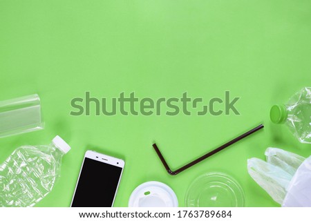 Top view of plastic garbage and smartphone on green background
