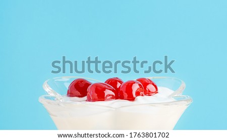 A dessert with maraschino cherry in a glass. Whipped cream, greek yogurt and ice cream on a blue background