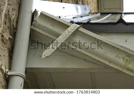 A rain gutter strap, with V notches, has pulled away from the house, letting the rain gutter fall.    Royalty-Free Stock Photo #1763814803