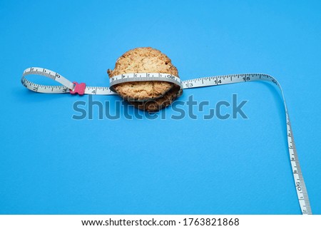 Jump rope handle tied up with measurement tape and oat cookies on blue background 