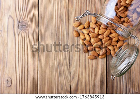 Almonds in a glass jar scattered on an old wooden table in cracks. Photo, image.