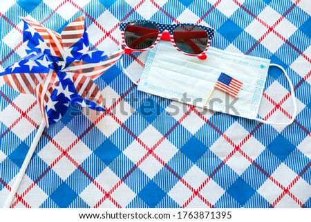 July 4 background. USA flags, sunglasses and medical mask on blue tablecloth. Independence Day of America during coronavirus covid-19 pandemic quarantine. Flat lay, top view, daylight. Copy space text