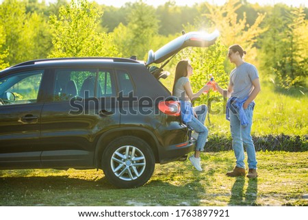 Beautiful young of a couple having romantic time drinking drinks in the car trunk on the sunset