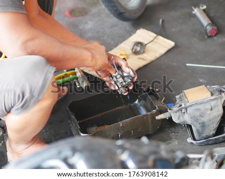 The man is repairing the carburetor of the motorcycle. A Serial.
