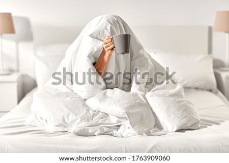 morning, comfort and people concept - young woman with cup of coffee sitting in bed under blanket at home bedroom Royalty-Free Stock Photo #1763909060