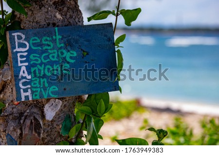 Wooden board on the beach with sea view with writing: Best Escape Anyone Can Have. Beautiful island Gili Air, Bali, Indonesia