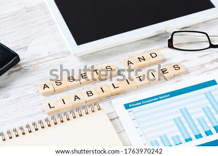 Assets and liabilities concept with letters on cubes. Still life of office workplace with supplies. Flat lay wooden desk with tablet computer and analytic report. Analysis of financial statements.