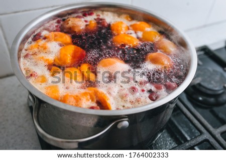 Fresh fruits are boiled in boiling water in a metal pan on the stove. Delicious stewed apricot, apples, cherries, raspberries. 