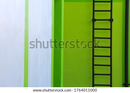 Black fire escape ladder on right frame with green and white cement walls. Blackground.