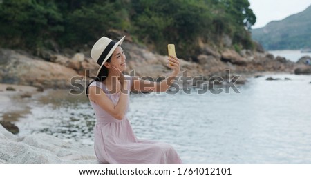 Travel woman takes selfie with cellphone and sits at seaside