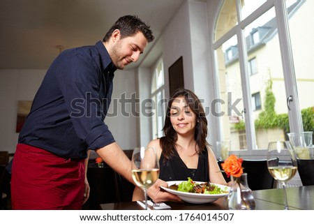 Friendly waiter brings salad to woman in restaurant