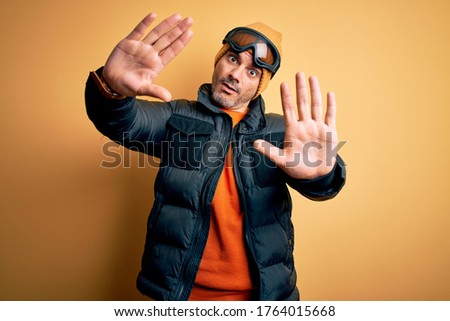 Young handsome skier man skiing wearing snow sportswear using ski goggles doing frame using hands palms and fingers, camera perspective