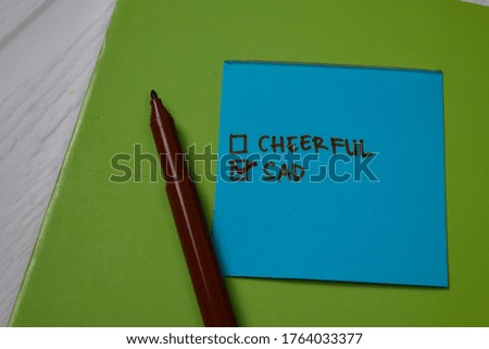 Cheerful and Sad write on a sticky note. Supported by an additional services isolated wooden table.