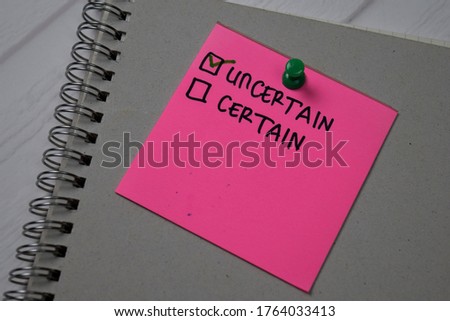 Uncertain and Certain write on a sticky note. Supported by an additional services isolated wooden table.