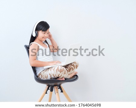 Little girl doing online class with laptop while sitting on chair at home.