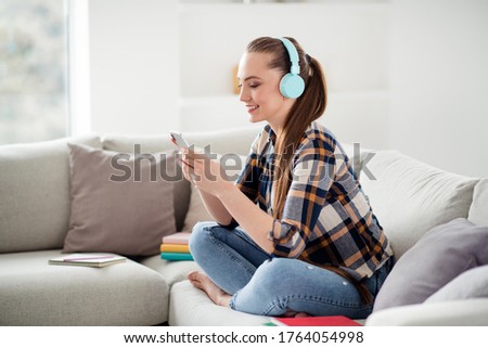 Profile photo of young cheerful lady student hold telephone hands sit sofa good mood listen youth music use earphones resting home remote social distance freelancer quarantine indoors