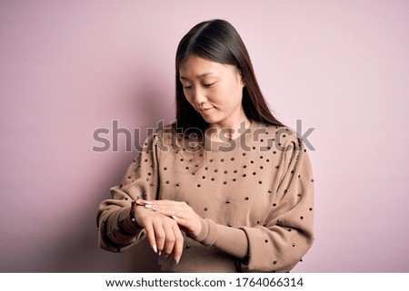 Young beautiful asian woman wearing fashion and elegant sweater over pink solated background Checking the time on wrist watch, relaxed and confident