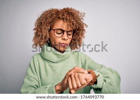 Young beautiful african american woman wearing turtleneck sweater and glasses Checking the time on wrist watch, relaxed and confident