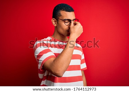 Young handsome african american man wearing casual striped t-shirt and glasses tired rubbing nose and eyes feeling fatigue and headache. Stress and frustration concept.