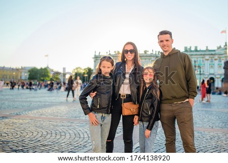 Family of four on the palace square in front of the popular museum with carriage of horses on background