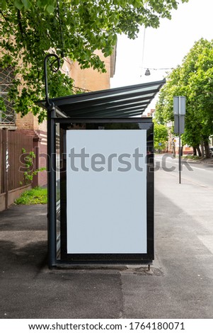 A large white blank advertising banner at a public transport stop of a trolley bus in the city on a background of trees. Vertical orientation.