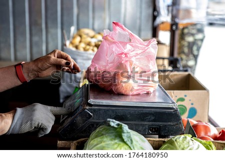 the seller of vegetables on market is weighing goods on scales for a buyer.