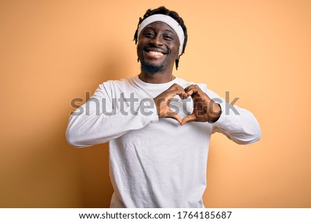 Young african american man doing sport wearing sportswer over isolated yellow background smiling in love showing heart symbol and shape with hands. Romantic concept.