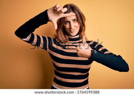 Young beautiful brunette woman wearing striped turtleneck sweater over yellow background smiling making frame with hands and fingers with happy face. Creativity and photography concept.