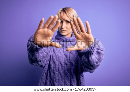 Young blonde woman with short hair wearing winter turtleneck sweater over purple background doing frame using hands palms and fingers, camera perspective