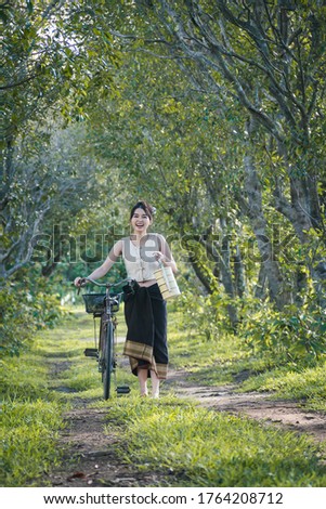 Picture with noise in over light ,Asia woman wearing traditional Thai dress holding food container and carry bicycle at countryside Thailand.