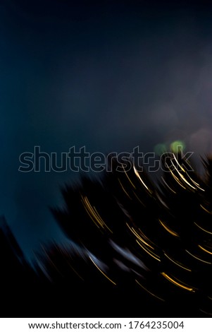 Abstract, motion-blurred, silhouetted bush with golden light-streaks under turquoise blue late evening sky with green and off-white hexagonal lens flares