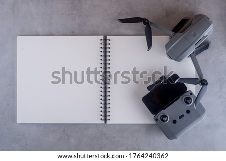 Blank notebook, drone, smartphone, controller on concrete table, from above.