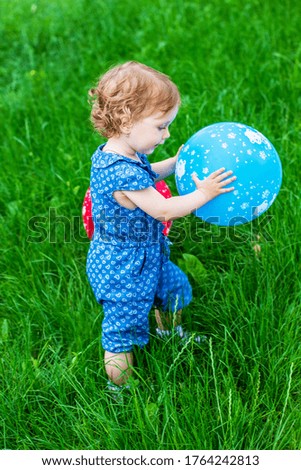 a little baby girl with a balloon in her hands on the green grass in a summer Park