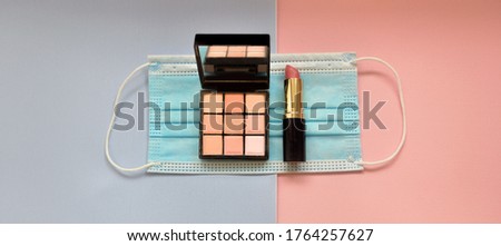 Shadow palette, lipstick and blue medical mask (protective mask) on a colored background. Flat lay, top view.