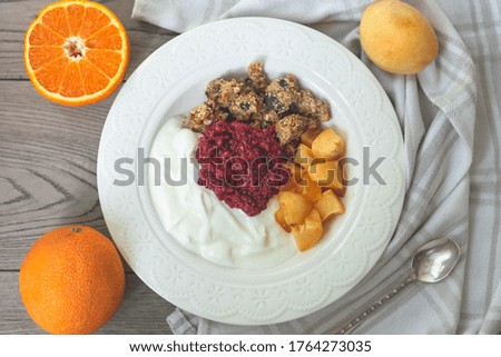 Healthy breakfast parfait of granola, greek yogurt, apricot and raspberry chia jam in a bowl. Fruits in the back