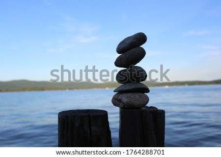 Artistic picture of stacked stones with background of lake, mountains, and sky