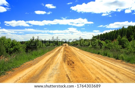 The road is dirt in the forest thicket, to green trees, with beautiful clouds.