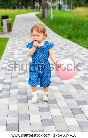 a little baby girl with a pink balloon in her hand runs along a path in a summer Park